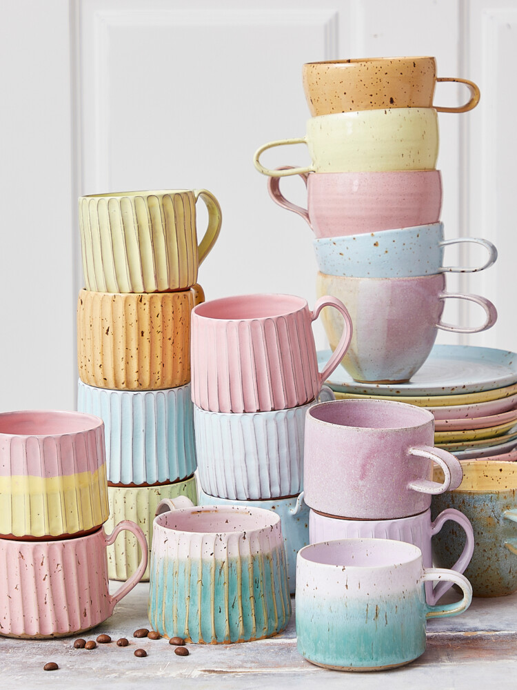 Keramikbecher und Tassen mit Griffen und Tassen ohne sie, rosa Keramikbecher, Karamellbecher in Pastell.